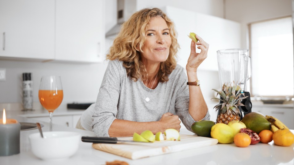 A woman in a grey top leaning over a counter with fresh fruit and a cutting board, eating cortisol-lowering foods