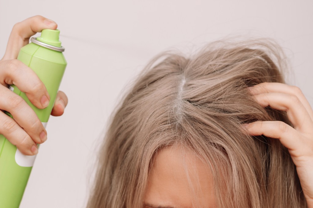 close up of woman spraying dry shampoo on scalp
