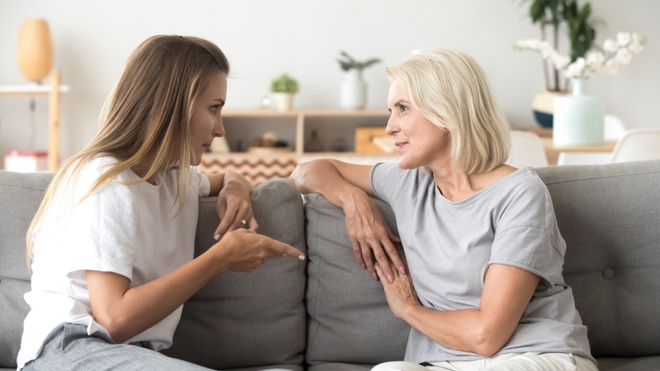 Middle aged woman sitting on sofa in living room with millennial female communicating at home. Mother and daughter spend time together talking having conversation. Warm trustful relationships concept