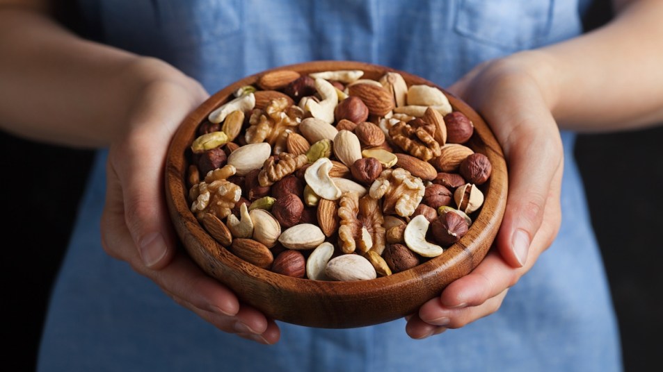 Woman's hands holding wooden bowl of mixed nuts