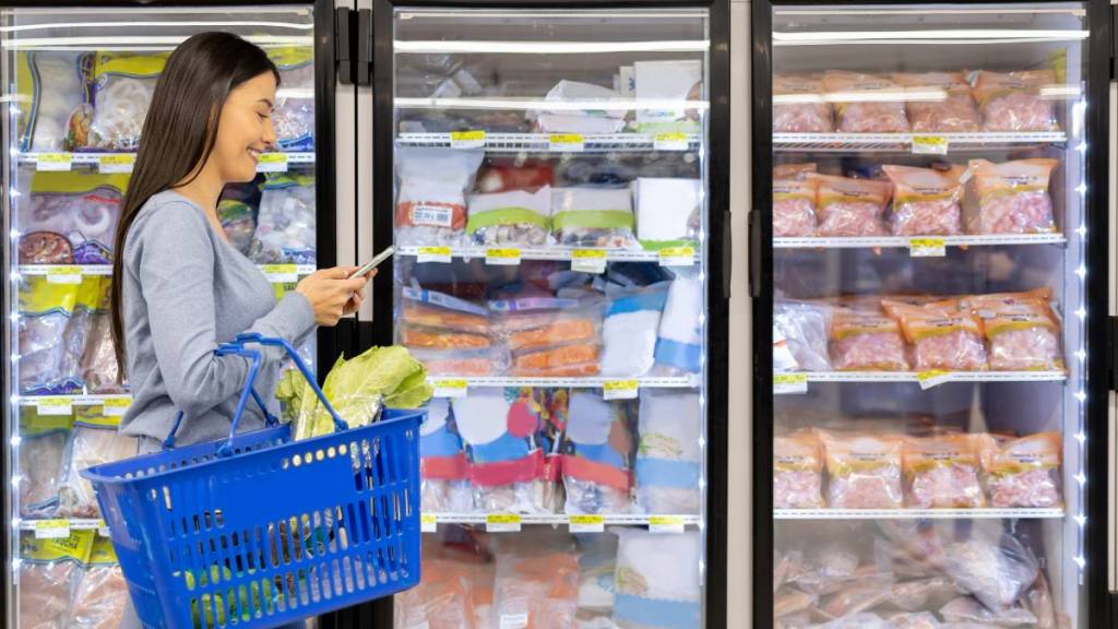 eat out for less: Latin American woman buying groceries at the supermarket and reading her shopping list on her cell phone - lifestyle concepts