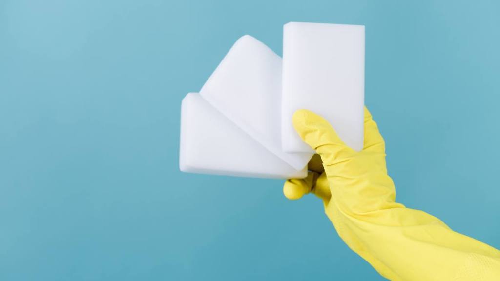 how to remove soap scum: Hand in a rubber yellow glove holding sponge on blue 
