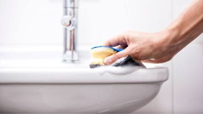 how to remove soap scum: Woman cleaning bathroom sink with sponge