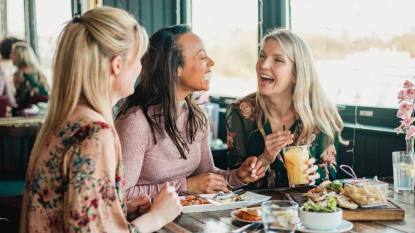 eat out for less: A front view shot of three beautiful mid-adult women enjoying brunch together in a restaurant, they are sitting around a table and laughing with eachother