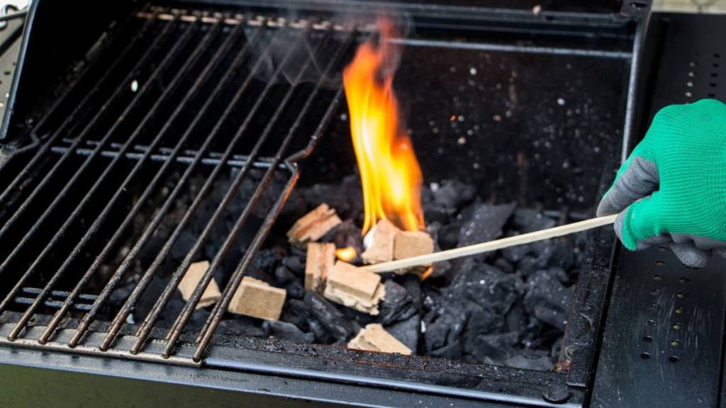 uses for sugar: Close up of a blazing match firing up a fire starting brick over a layer of charcoal inside a barbecue fireplace