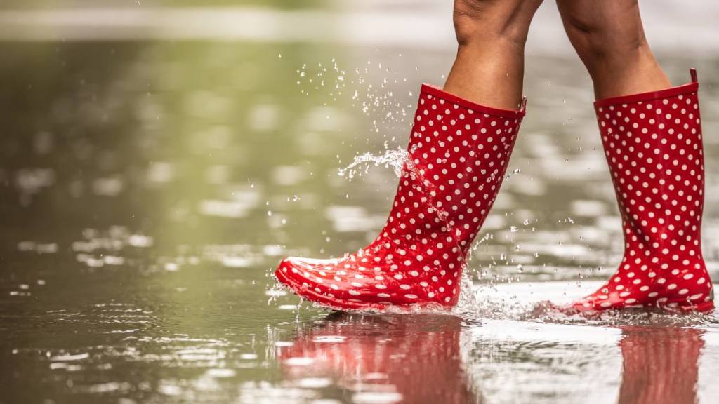 woman in rain boots stepping in puddle ; happy and healthy