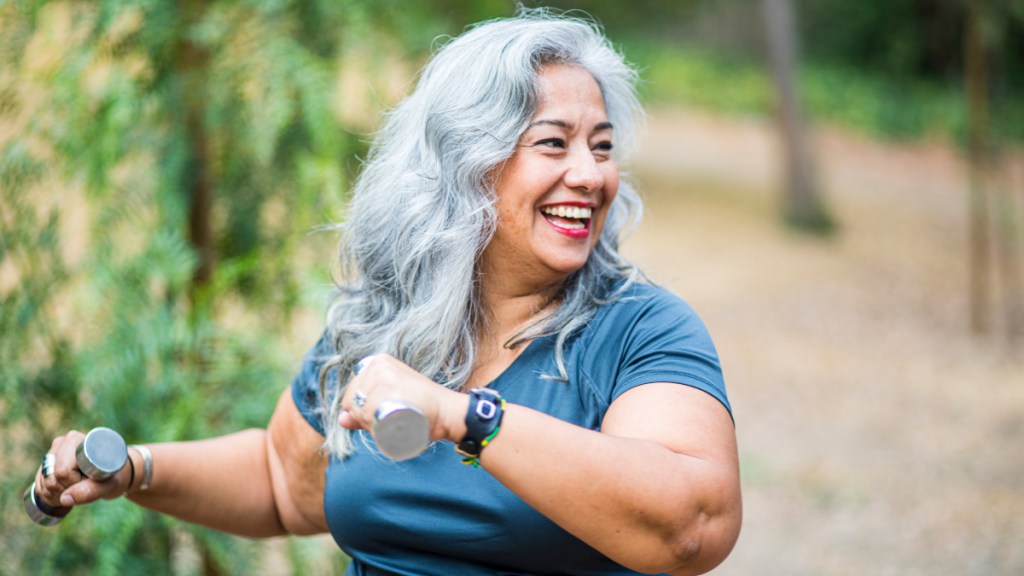 A woman with long grey hair holding hand weights to exercise
