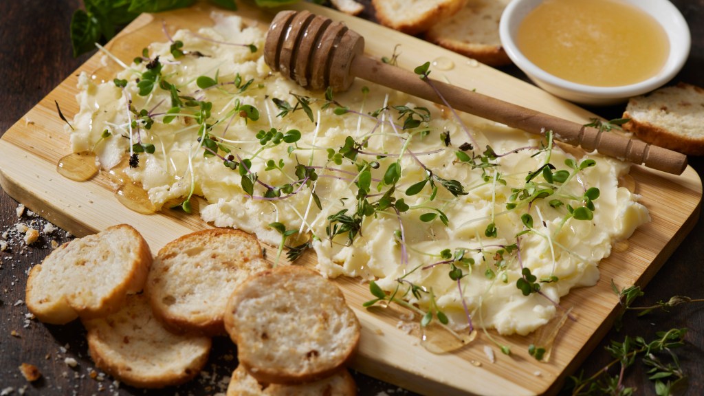 Snacks for St Patrick's Day: Viral Butter Board made by spreading butter onto a wooden cutting board, then topping with honey and microgreens and serving alongside sliced, toasted bread for dipping