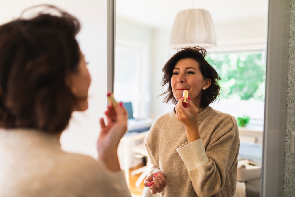 mature woman applying lip balm in mirror