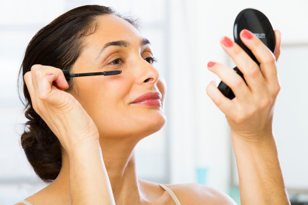 mature woman applying mascara in mirror