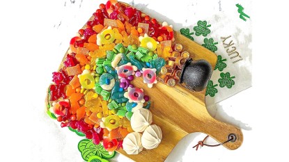 Snacks for St Patrick's Day: Colorful gummy candy, Rolo candies, meringues and a mini plastic cauldron arranged on a wooden cutting board to look like a rainbow with clouds at one end and a pot of gold at the other