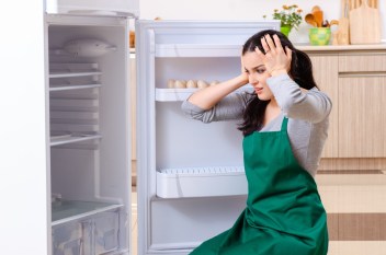Woman sitting in front of refrigerator, frustrated