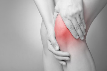 Black and white photo of woman with knee pain, with knee colored in red