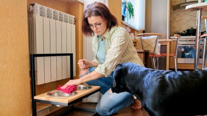 Woman sitting on floor cleaning dog food bowl as dog looks on