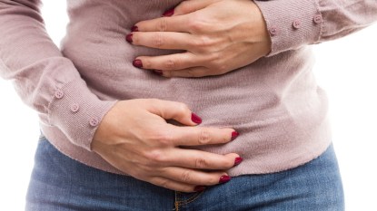woman with red nails holding her stomach, feeling bloated