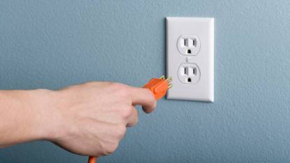 Does unplugging appliances save electricity: Hand plugging power cord into outlet