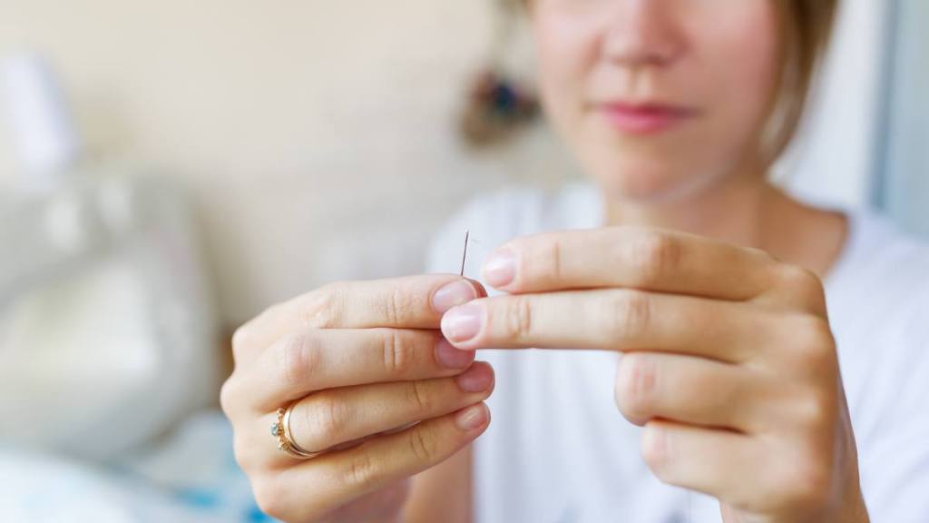 Uses for clear nail polish: A young seamstress works with a needle and thread. Selective focus in needle