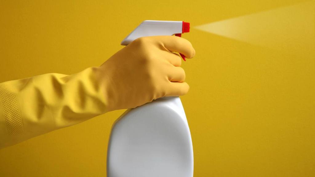 Uses for Pantyhose: Hand in yellow rubber glove helds a plastic spray bottle with cleaning detergent on a yellow background.