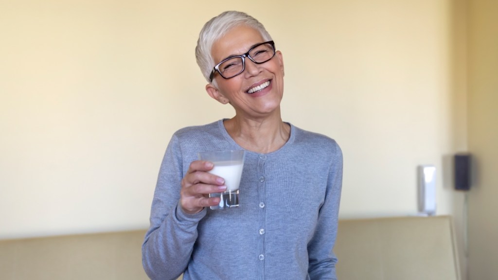 A woman wearing glasses while holding a glass of milk and smiling