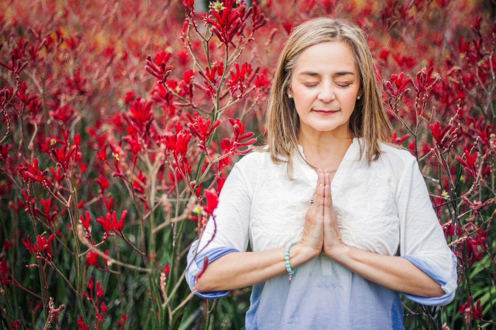 Woman showing hopefulness by praying outside surrounded by red flowers
