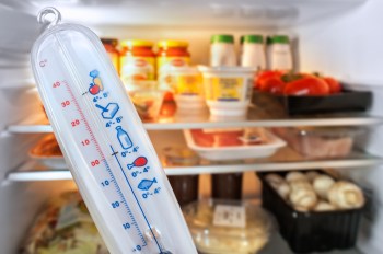 Thermometer in front of open refrigerator filled with food