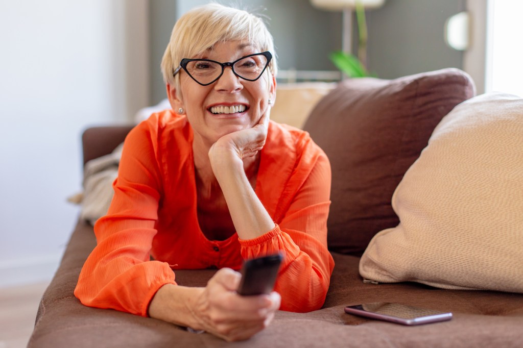 Woman feeling hopefulness as she smiles and holds remote control on couch
