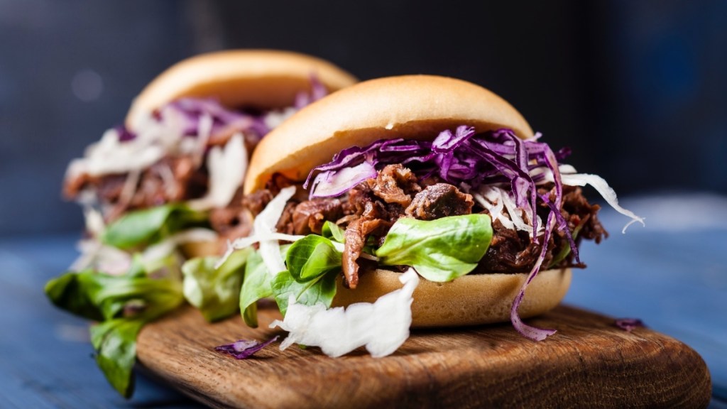 A bun filled with jackfruit "pulled pork" and cabbage on a wooden tray