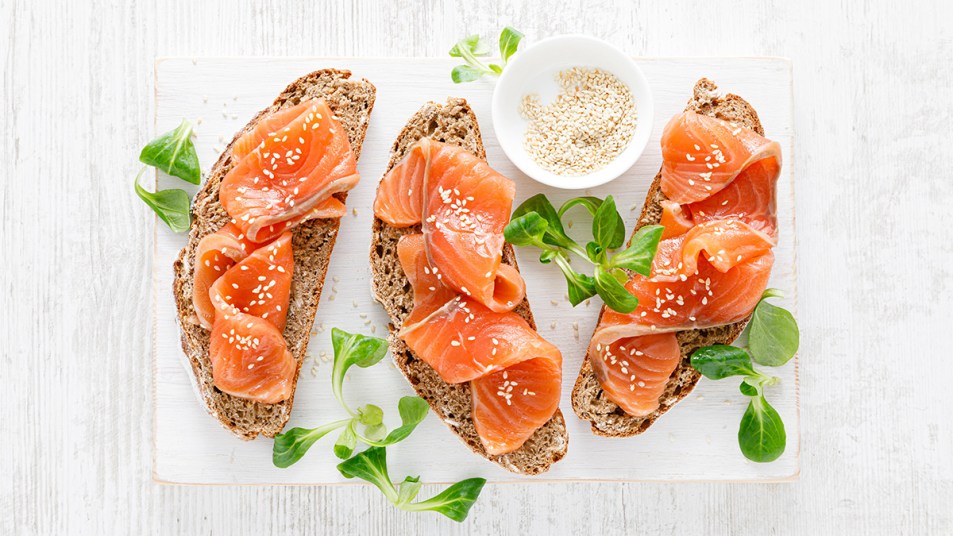 Whole grain rye bread open sandwiches with salted salmon on a white rustic wooden table