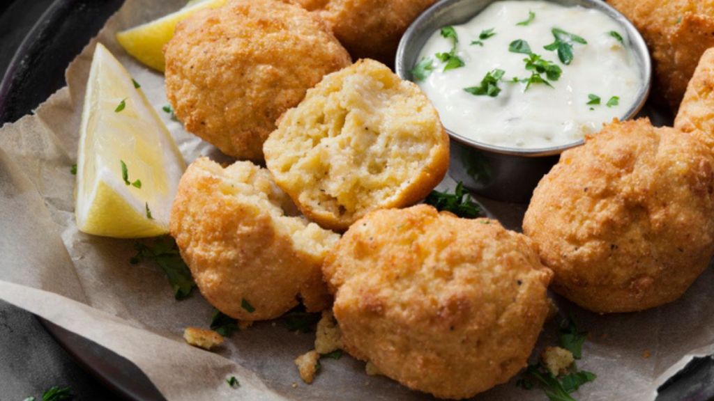 air fryer hush puppies recipe: halved hush puppy next to others in basket with dipping sauce