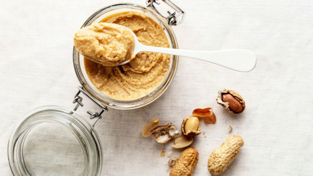 homemade nut butter: peanut butter in jar with peanut shells on white background