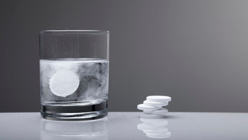 overnight cleaning hacks: denture tablet fizzing in glass of water next to stack of tablets 