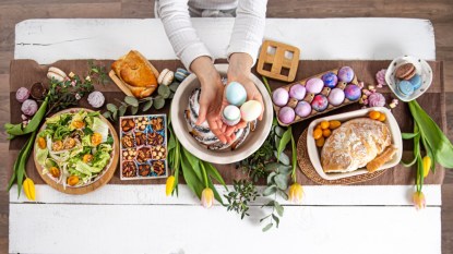 Woman's hands setting Easter table with eggs, flowers, and a variety of foods
