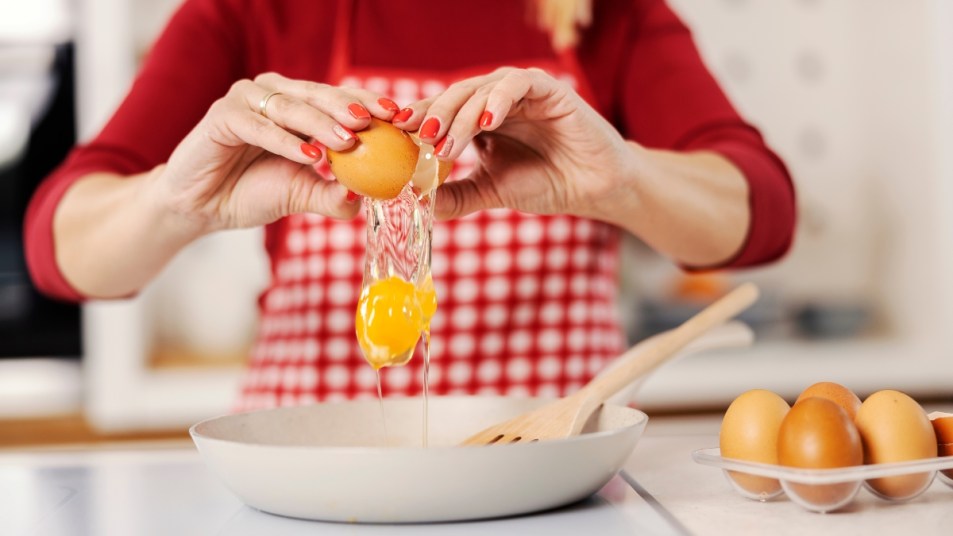 close shot of blonde woman in red sweater and red checkered apron cracking an egg into a bowl