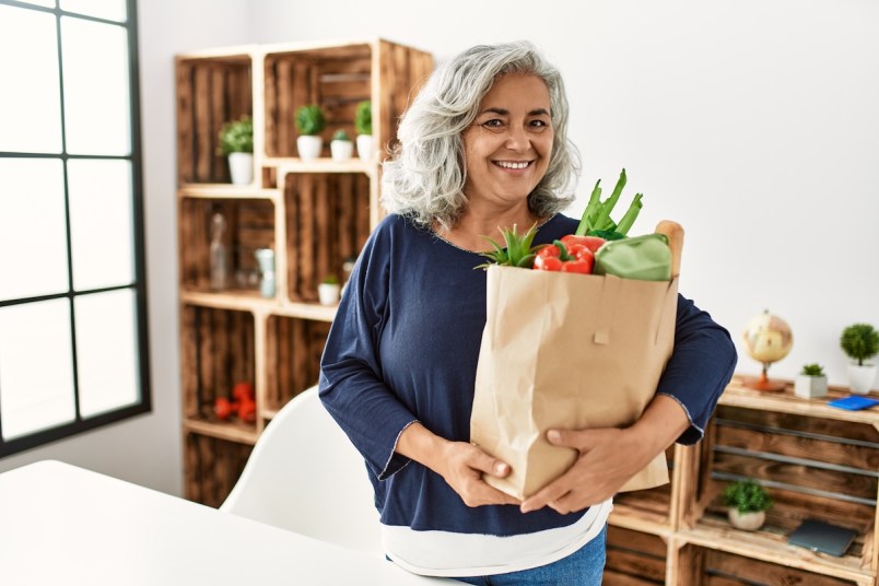 Woman smiling as she holds a paper bag filled with groceries