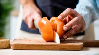 how to sharpen knives: Hands of woman slicing tomato on cutting board