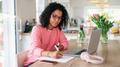 Work from home airline jobs: Young multiracial woman with black curly hair having home office in kitchen, writing notes.