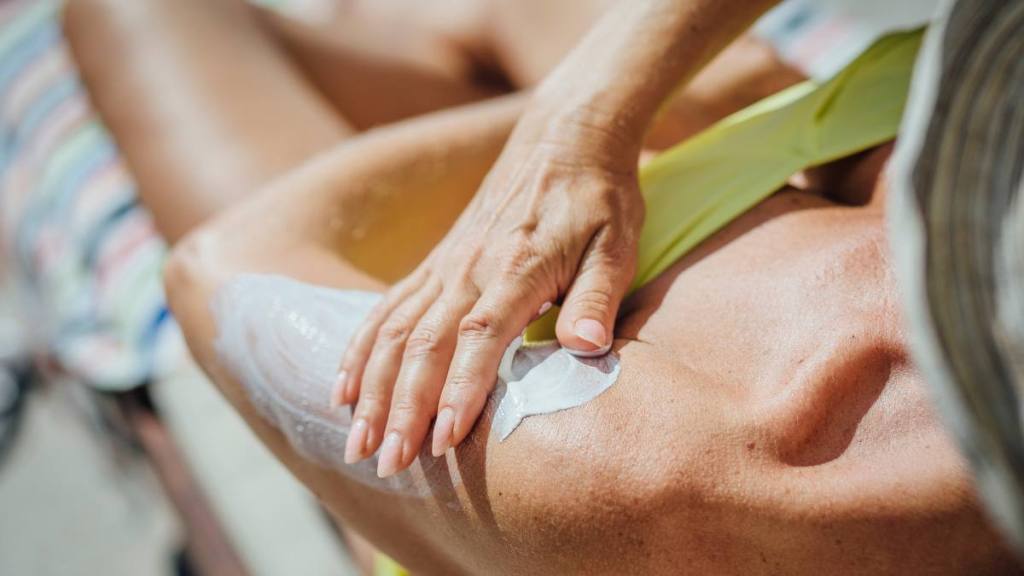 uses for shaving cream: Mature woman lying on a deck chair by the pool on holiday. She is rubbing sun lotion into her arm.