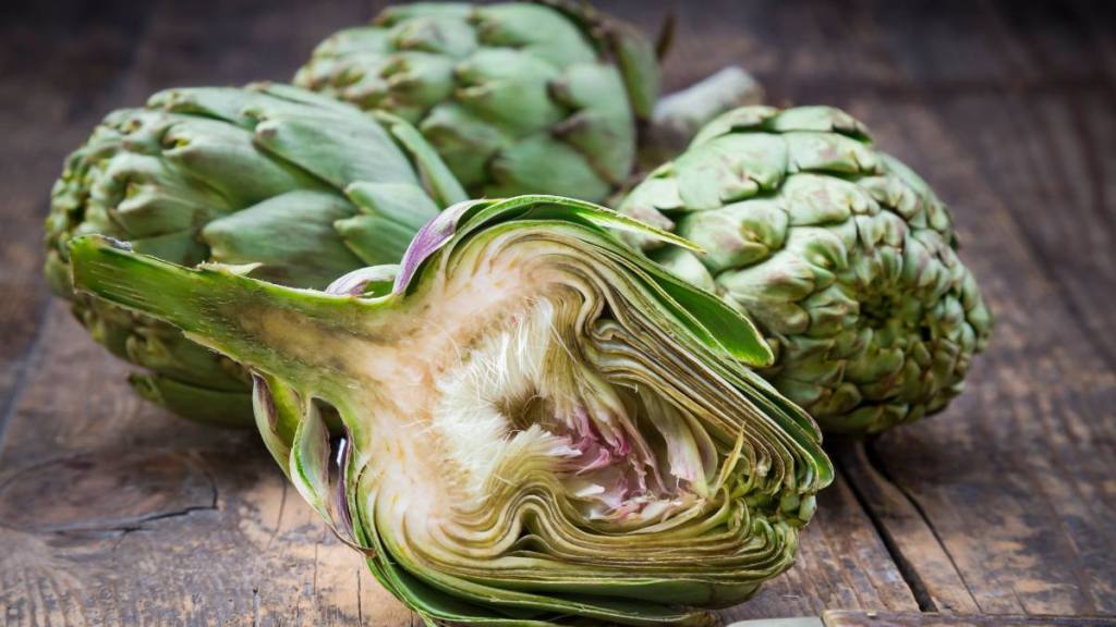 Sliced and whole organic artichokes and kitchen knife on wooden table