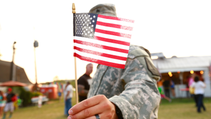 U.S. veteran holding American flag wearing military uniform.