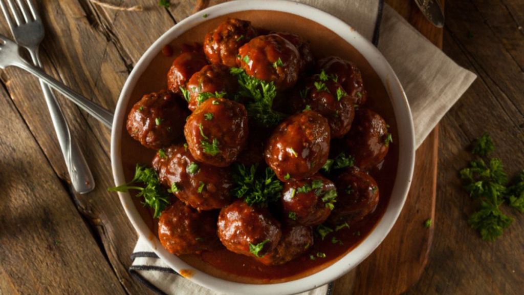 bourbon meatballs with herbs in white serving bowl with utensils