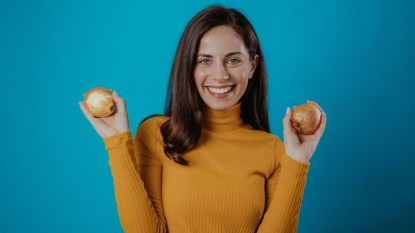 smiling woman holding two onions for surprising uses for onions