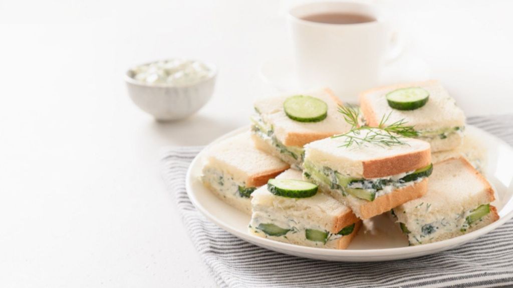 cucumber tea sandwiches piled on white plate with tea