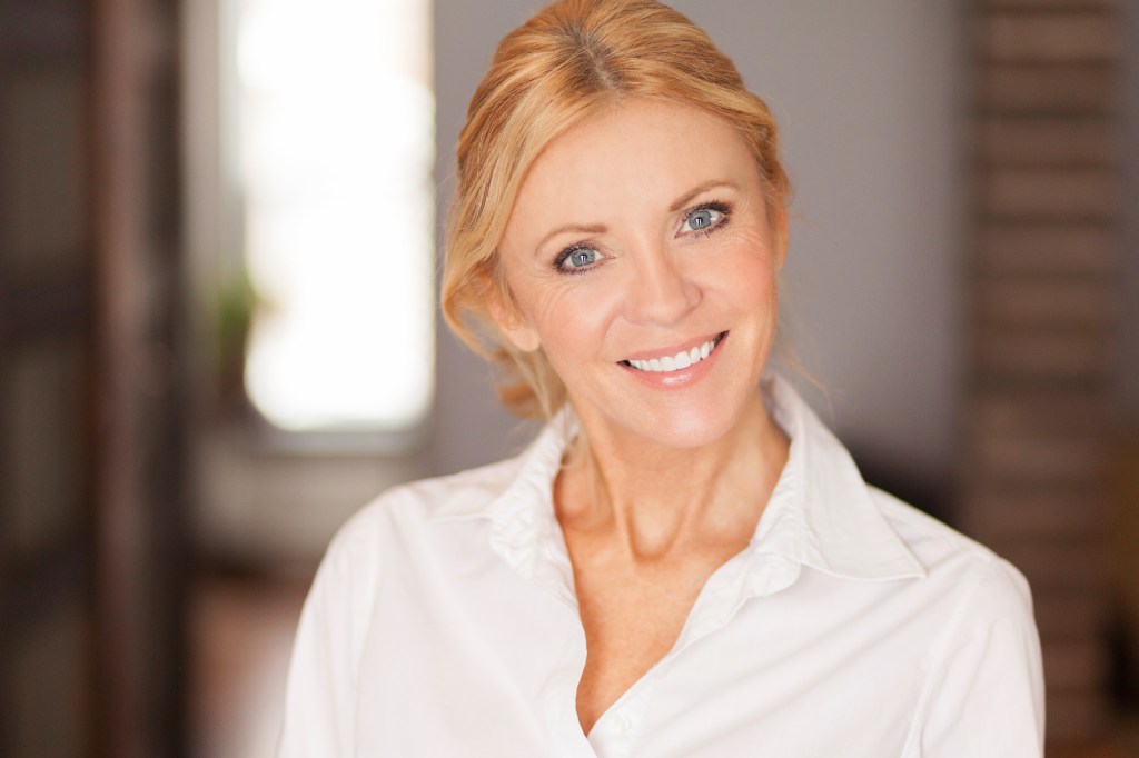 A closeup of a blonde woman wearing a white button up that's smiling