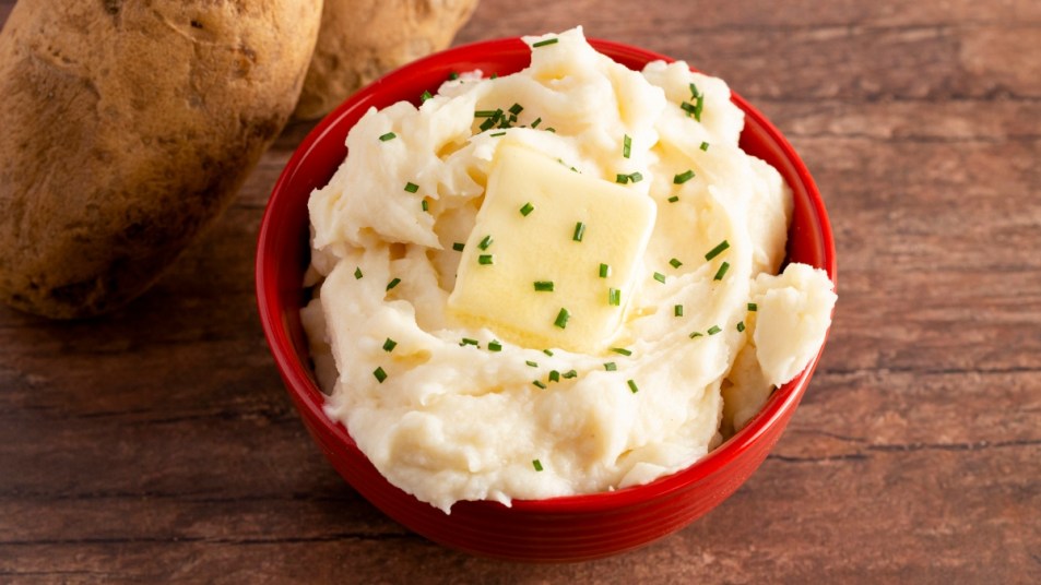 Mashed potatoes with butter and chives in a red bowl on a wood table