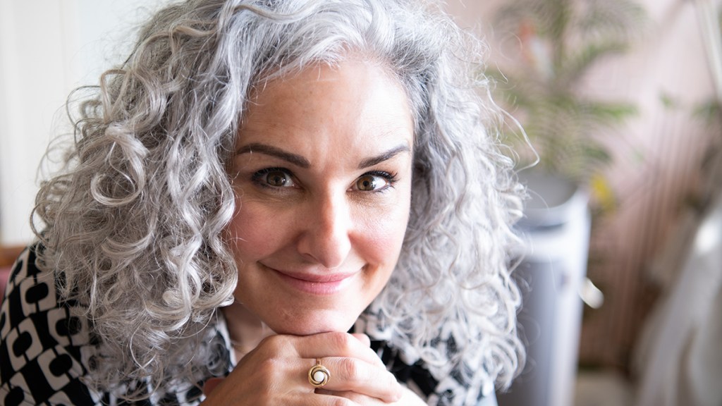 A woman with gray curling hair who has styled her thinning hair so it looks thicker