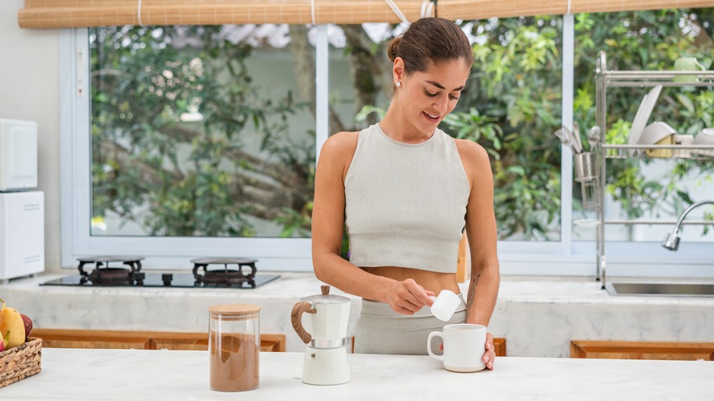 A healthy woman adding protein powder to her coffee to help with weight loss