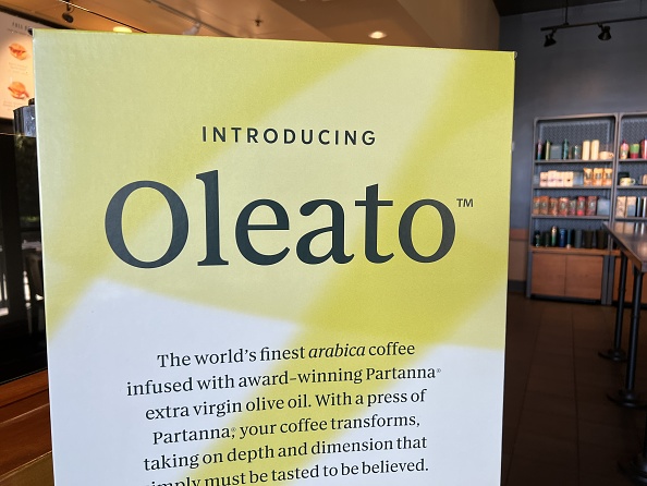 A stand-up yellow sign at Starbucks promoting their new Oleato line of drinks. It reads: "Introducing Oleato. The World's finest arabica coffee infused with award-winning Partanna extra virgin olive oil. With a press of Partanna, your coffee transforms, taking on depth and dimension that simply must be tasted to believed."