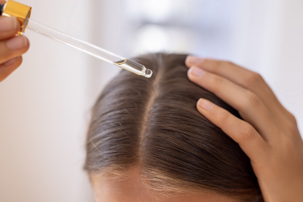 Woman applying oil onto scalp using dropper.