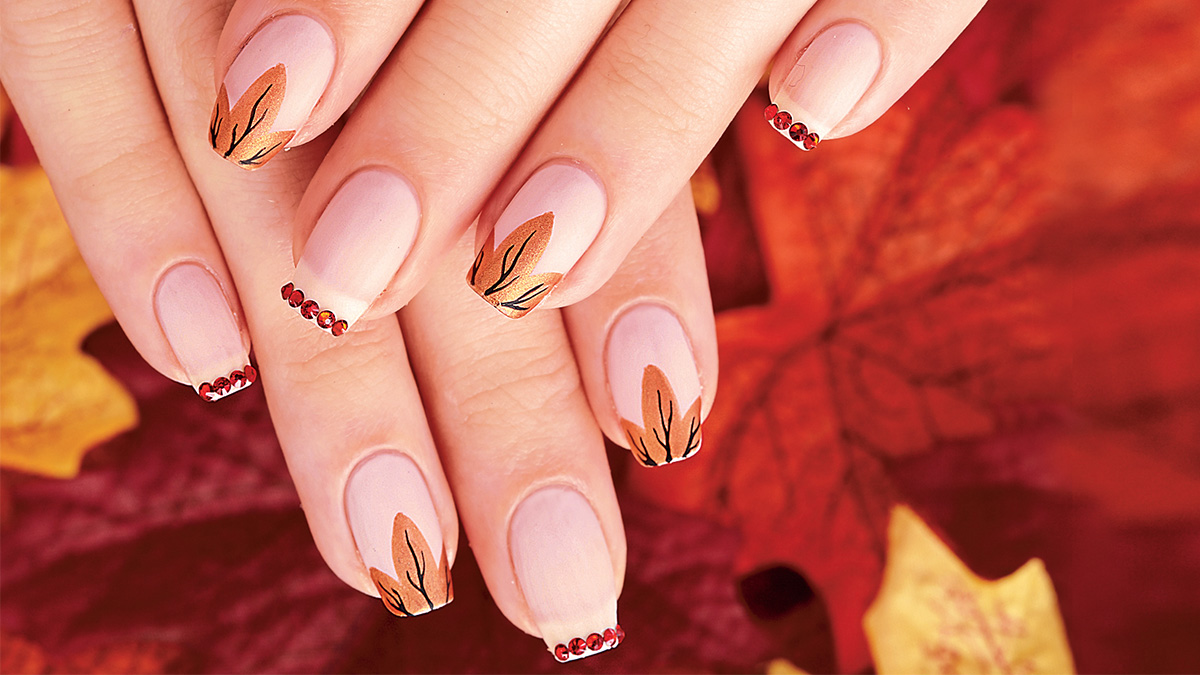 Nails painted with leaf French tips and red rhinestones on top of a leaf background