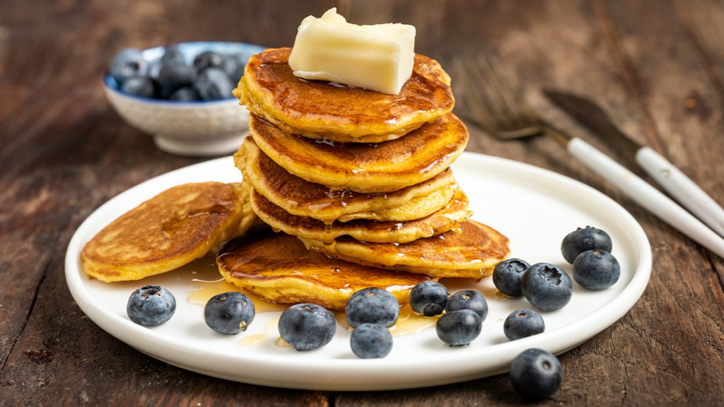 Stack of mini pancakes made from muffin mix, topped with blueberries, syrup and a pat of butter